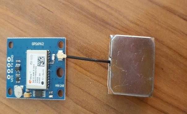The GPS module on a wooden table: a small circuit board with its antenna wired to a flat metal patch. Photographed in 2022 and tinted amber.